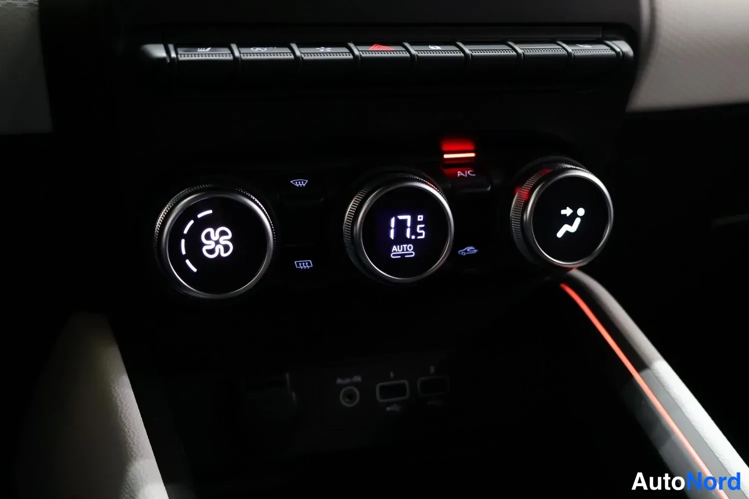 Yksityiskohta: Ilmastoinnin kolme pyöreää säädintä: keskimmäinen näyttää lämpötilan 17,5 ja AUTO-tilan, vieressä A/C-painike valolla; alla USB-portit ja 12V-pistoke.