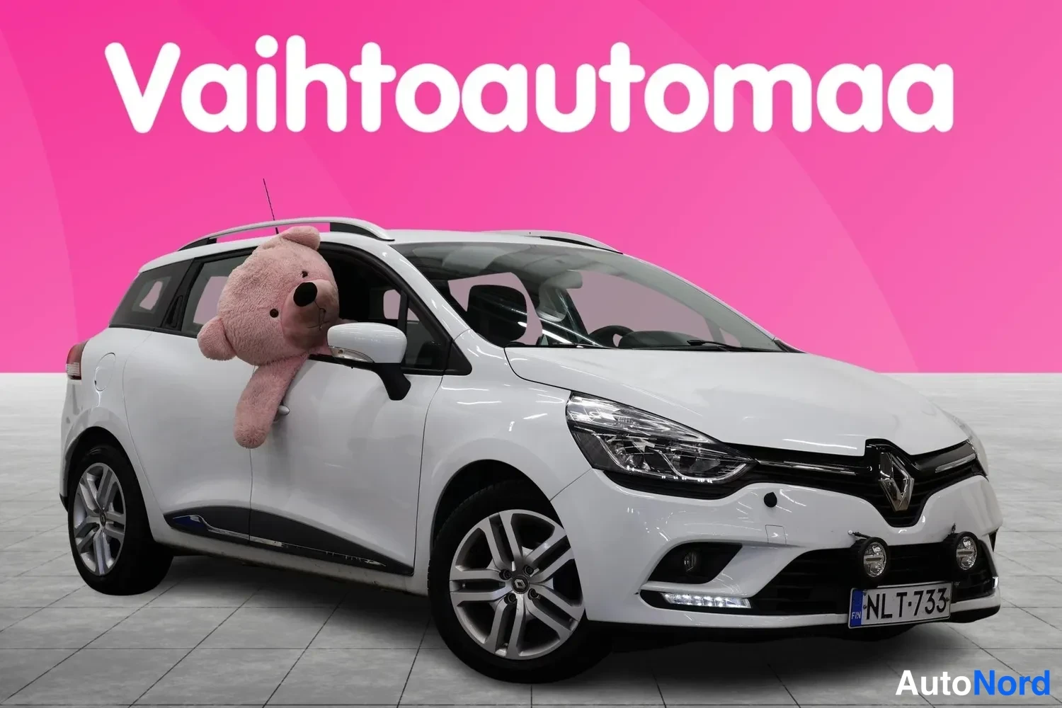 Etuviisto, nokka oikealle: Valkoinen Renault Clio Sport -farmari kolmosen nurkasta, etusuunta oikealle, pehmolelu takapenkiltä ikkunasta.