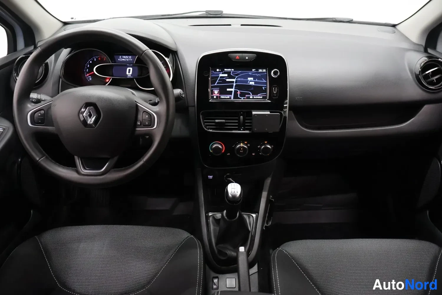Yksityiskohta: Ohjaamo kohtisuoraan: Renault-ohjauspyörä, mittaristo ja kosketusnäytöllinen radiokeskus, manuaalivaihteisto ja tummat istuimet.