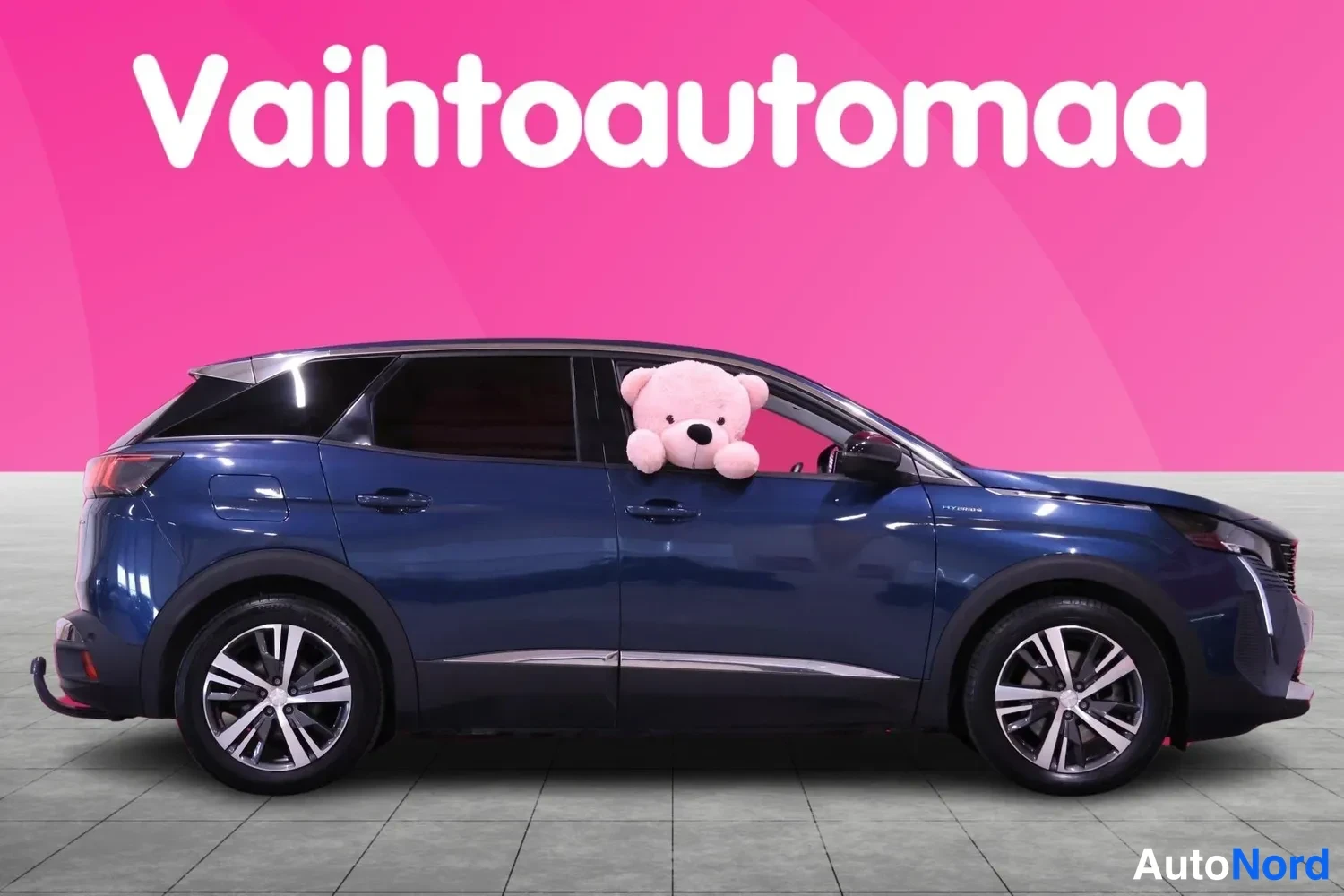 Etuviisto, nokka oikealle: Tummansininen farmillinen henkilöauto kylki näkyvissä, keula oikealla reunalla, pehmolelu ikkunasta pilkottaa.