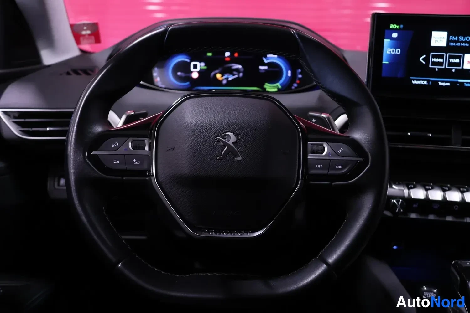 Muu: Peugeot-logolla varustettu ohjauspyörä lähikuvassa; ääniohjauksen ja puhelun painikkeet, taustalla mittaristo ja näyttö.