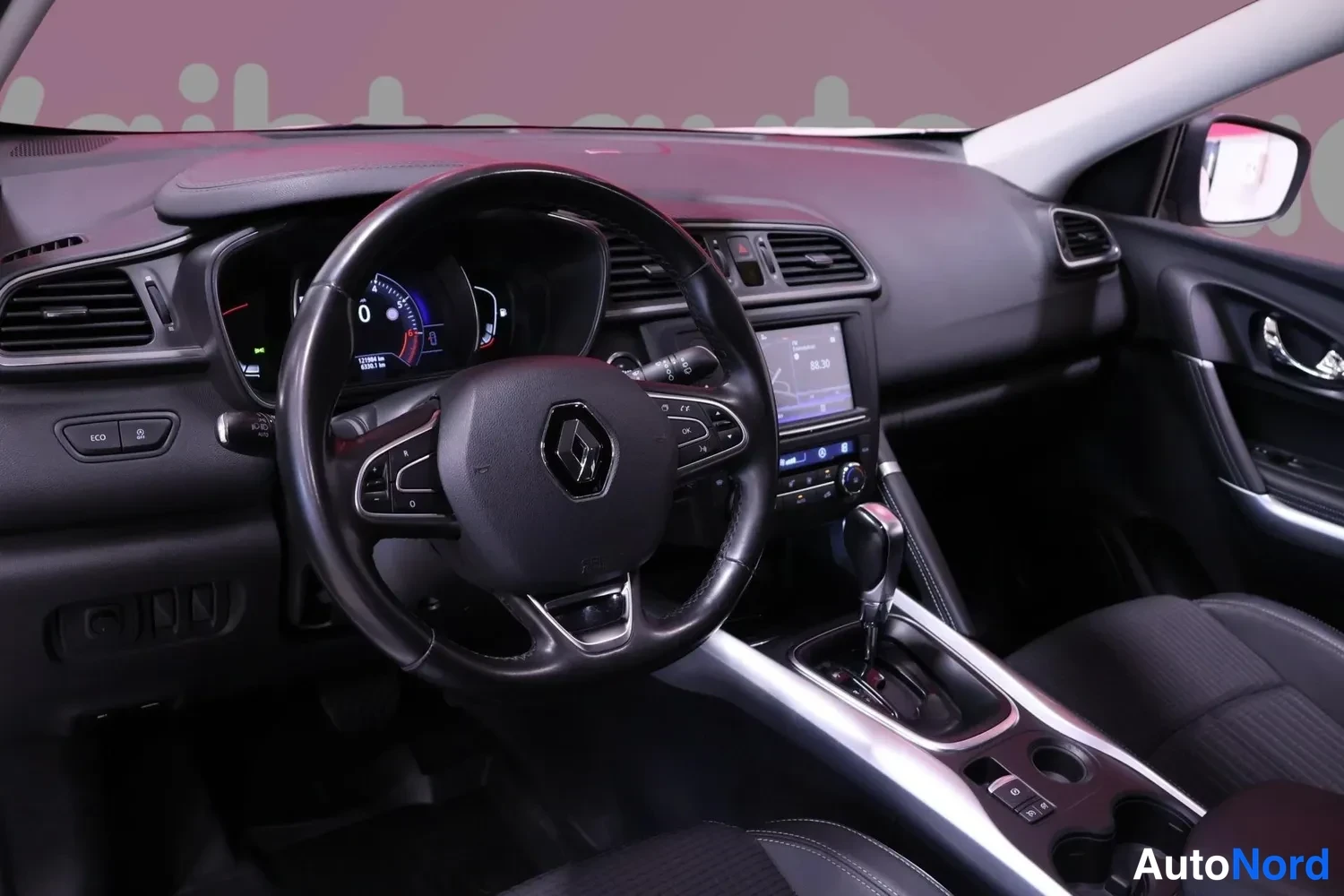 Muu: Renaultin ohjaamo edestä: musta ohjauspyörä logoineen, digitaalinen mittaristo, kosketusnäytöllinen radio ja automaattivaihteiston valitsin keskikonsolissa.