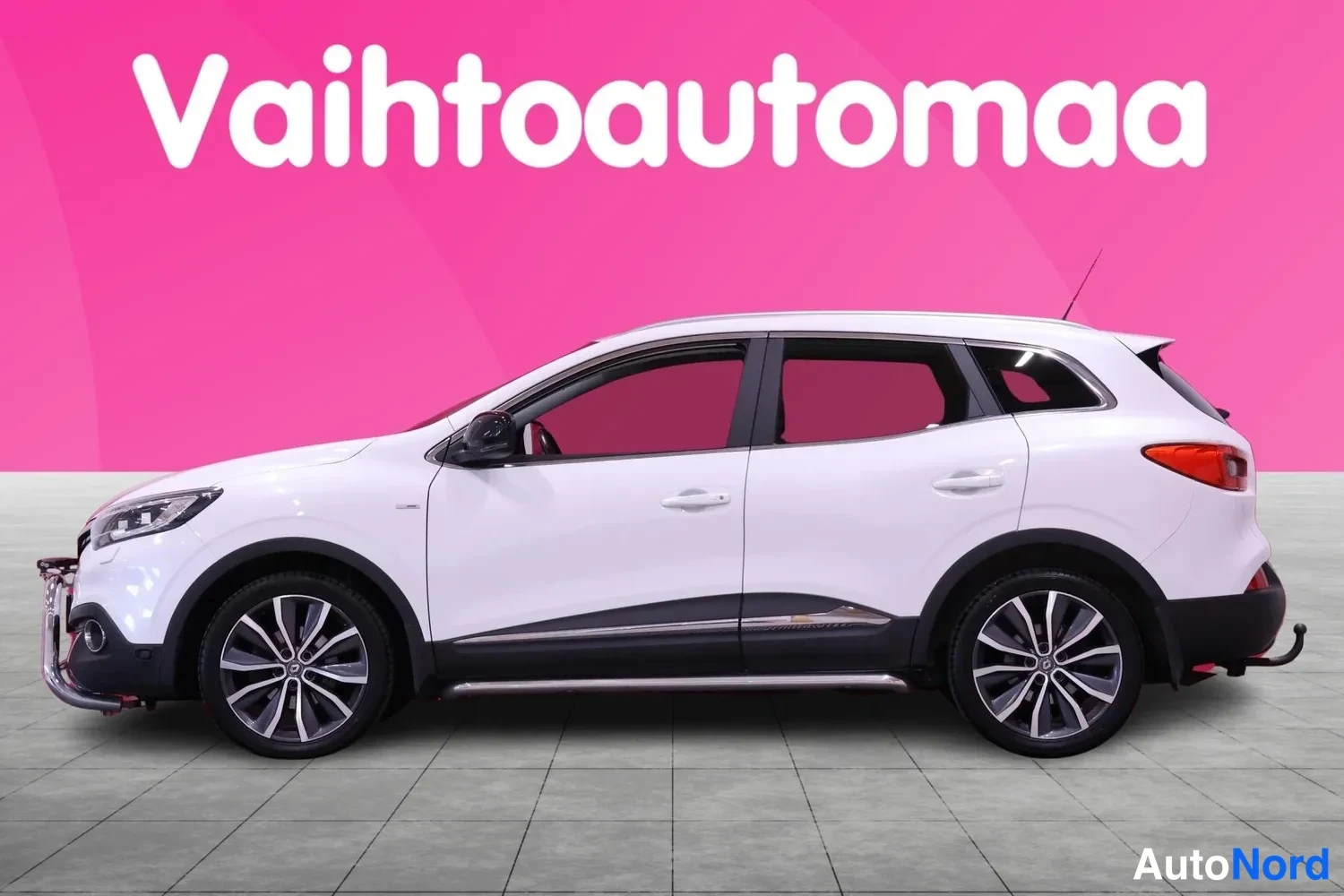 Etuviisto, nokka vasemmalle: Valkoinen Renault Kadjar vasemmalta viistosti edestä, ajoneuvossa etusuoja ja listat ovien alapuolella.