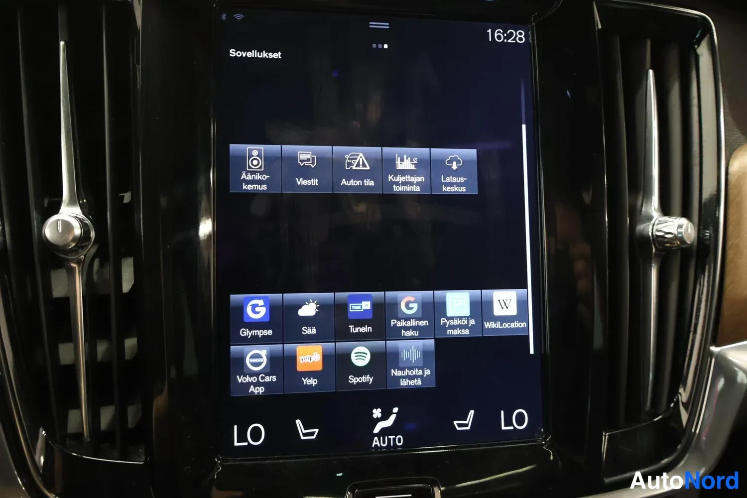 Muu: Keskikonsolin infotainment-näyttö, jossa Sovellukset-valikko sovelluskuvakkeineen ja alarivissä istutinlämmityksen ja AUTO-ilmastoinnin säädöt.