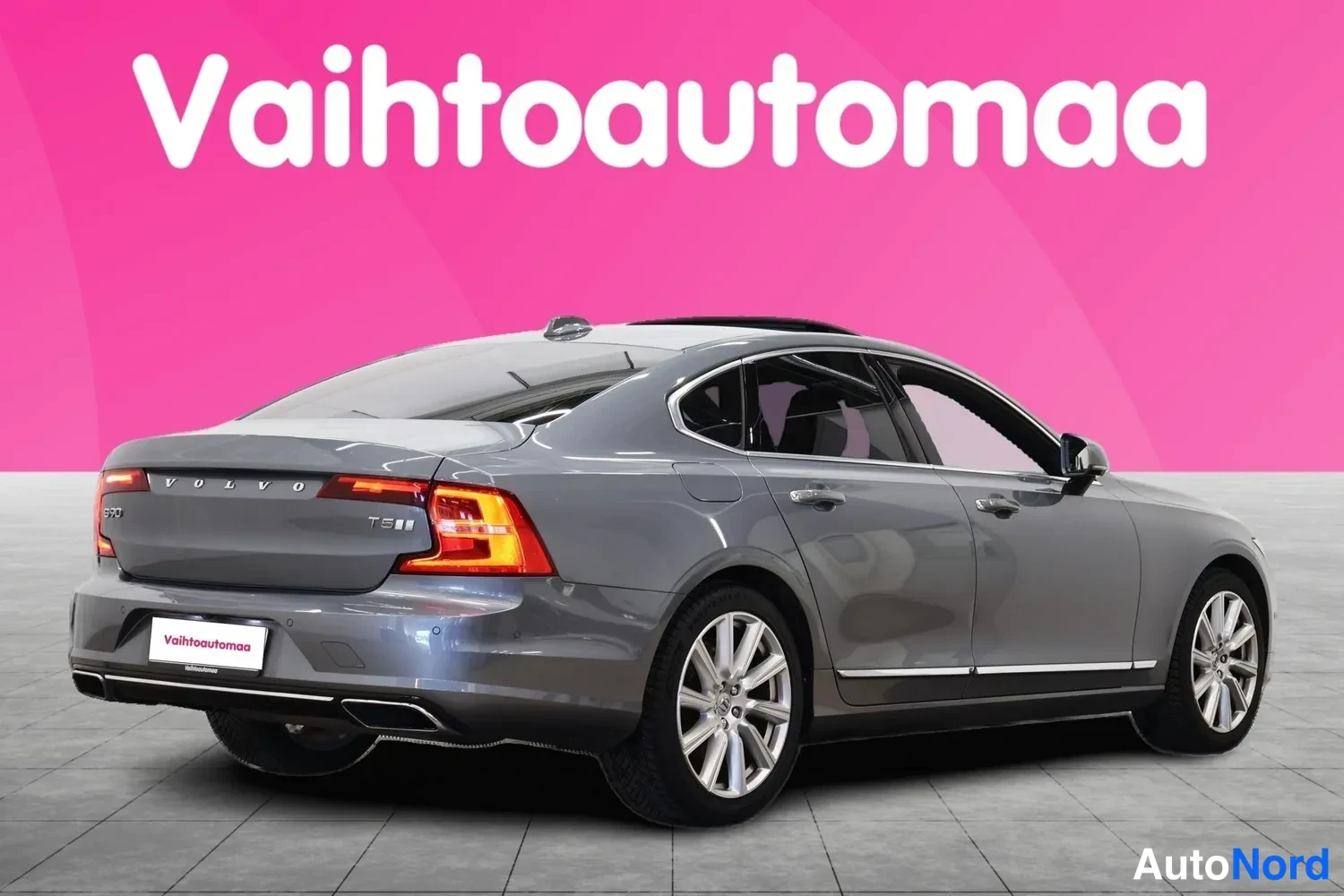 Takaviisto: Volvo S90 -sedanin takakulmanäkymä harmaana pinkkivalkoisella studiotaustalla, takavalot ja V O L V O -teksti näkyvissä.