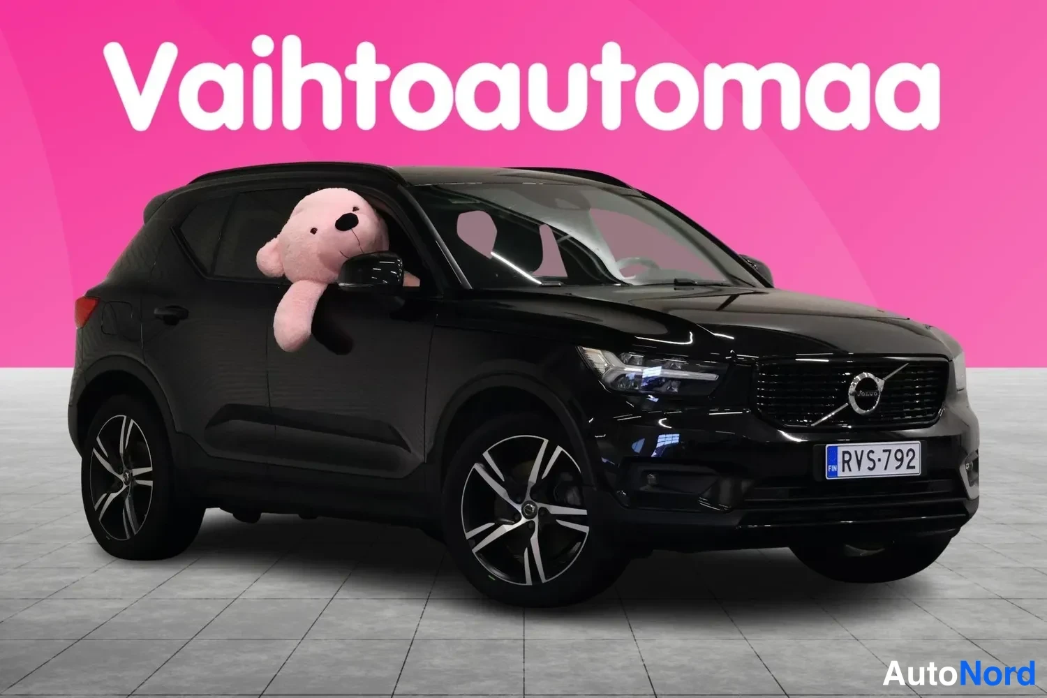 Etuviisto, nokka oikealle: Musta Volvo XC40 etuviistosta oikealta, pehmolelu takanäytössä