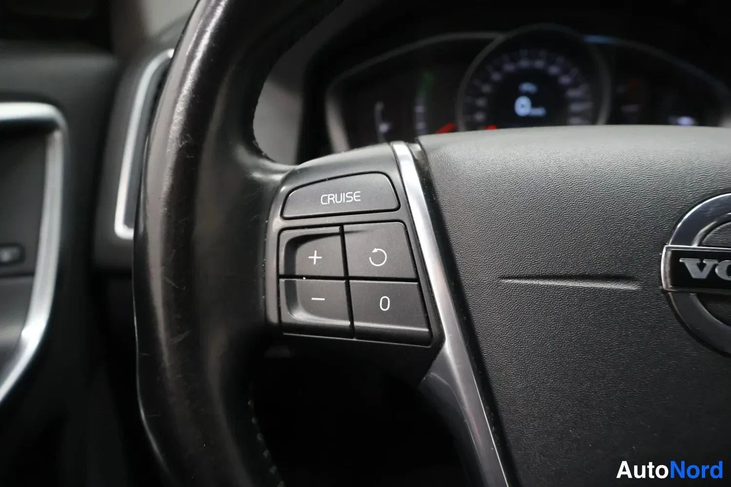 Muu: Volvo-ohjauspyörän vasen puhelinpainikesarja, jossa CRUISE-nappi sekä plus-, miinus- ja nollauspainikkeet, taustalla rajoitetusti mittaristo.