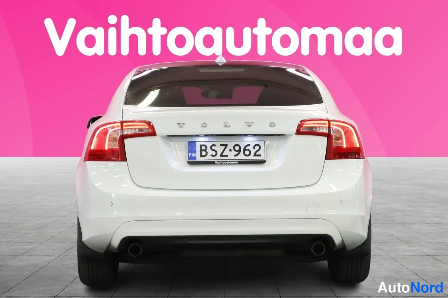Takaa: Auton takaosa suoraan takaa: valkoinen sedan, VOLVO-teksti ja rekisterikilpi, punaiset takavalot ja kaksi pakoputkea.