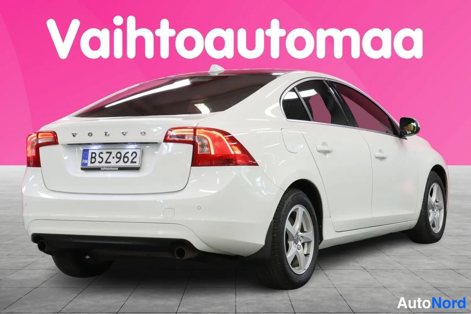 Takaviisto: Valkoinen sedan kolmesta neljäsosaan takaa oikealta: takavalot, VOLVO-teksti, kilpi ja oikean puolen korirakenteet ja pyörät.