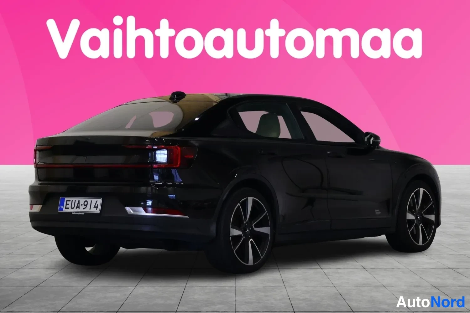 Takaviisto: Mustan hatchbackin takaosa kolmannelta suunnalta, rekisterikilpi, vaaleanharmaa lattia ja vaaleanpunainen tausta.