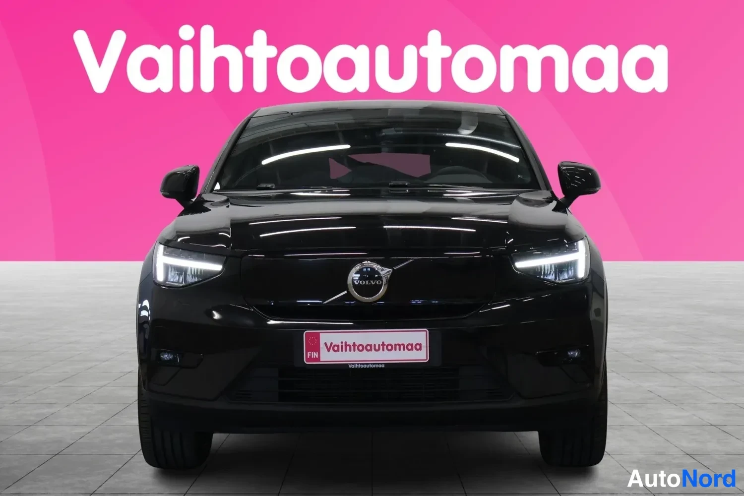 Edestä: Etukatselma mustasta Volvo C40 -autosta, LED-ajovalot päällä ja Vaihtoautomaan rekisterikilpi.