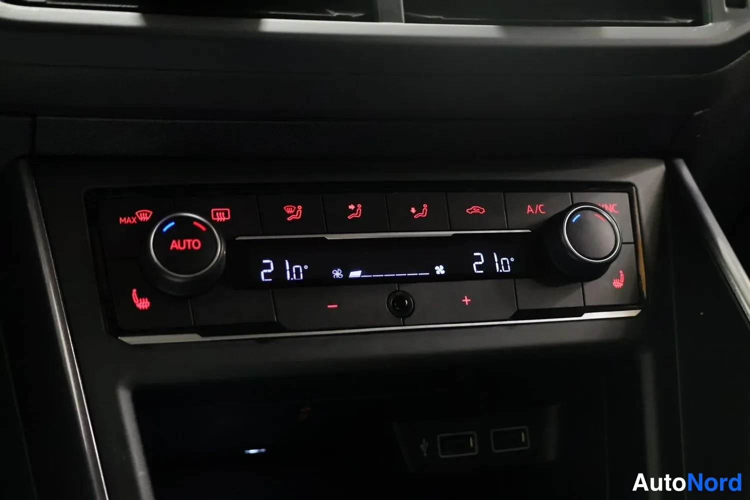 Muu: Volkswagenin keskikonsolin automaattinen ilmastointipaneeli, jonka näytössä on kaksi lämpötilaa 21,0°, A/C-merkintä, AUTO-nappi ja istuinten lämmityspainikkeet.