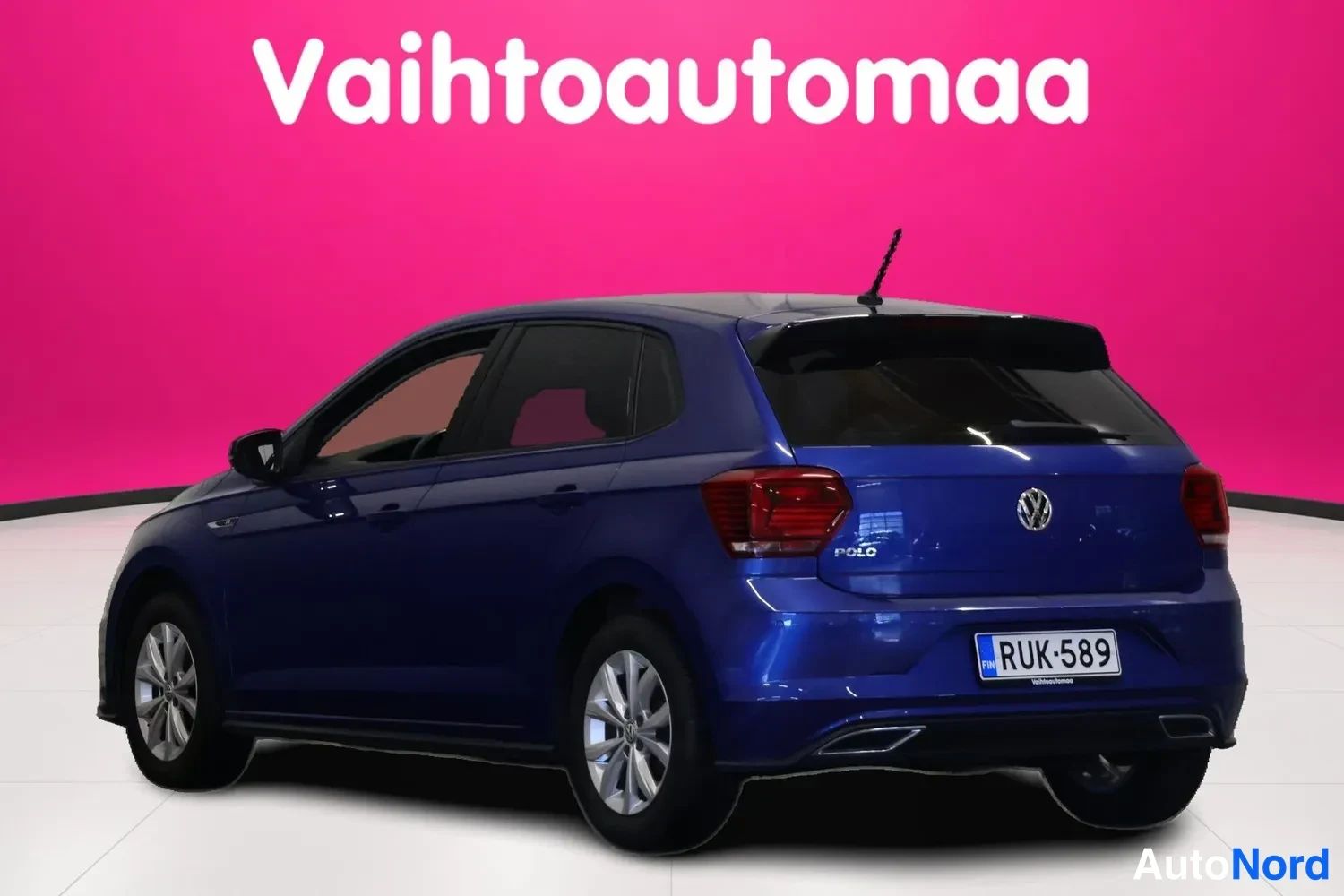 Takaviisto: Sininen Volkswagen Polo takaviistosta vasemmalta valkoisella studio-lattialla, rekisterikilpi.