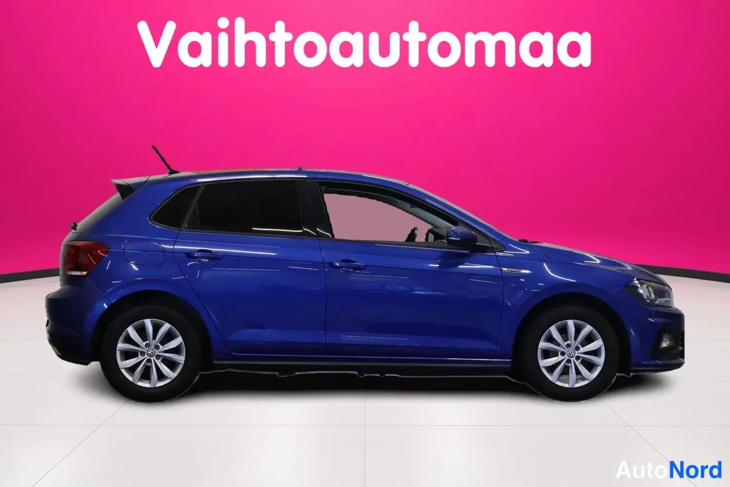 Sivulta: Sininen Volkswagen Polo kokonaan sivulta oikealta nähtynä vaaleanpunaisella taustalla.