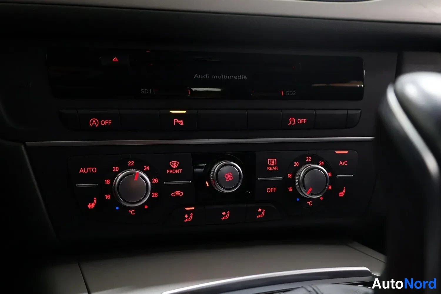 Yksityiskohta: Kesk consolin ilmastointipaneeli, jossa on AUTO, A/C, FRONT ja REAR -painikkeet, kaksi säädintä ja lämpötilan asteikko, näytön yläpuolella teksti 'Audi multimed