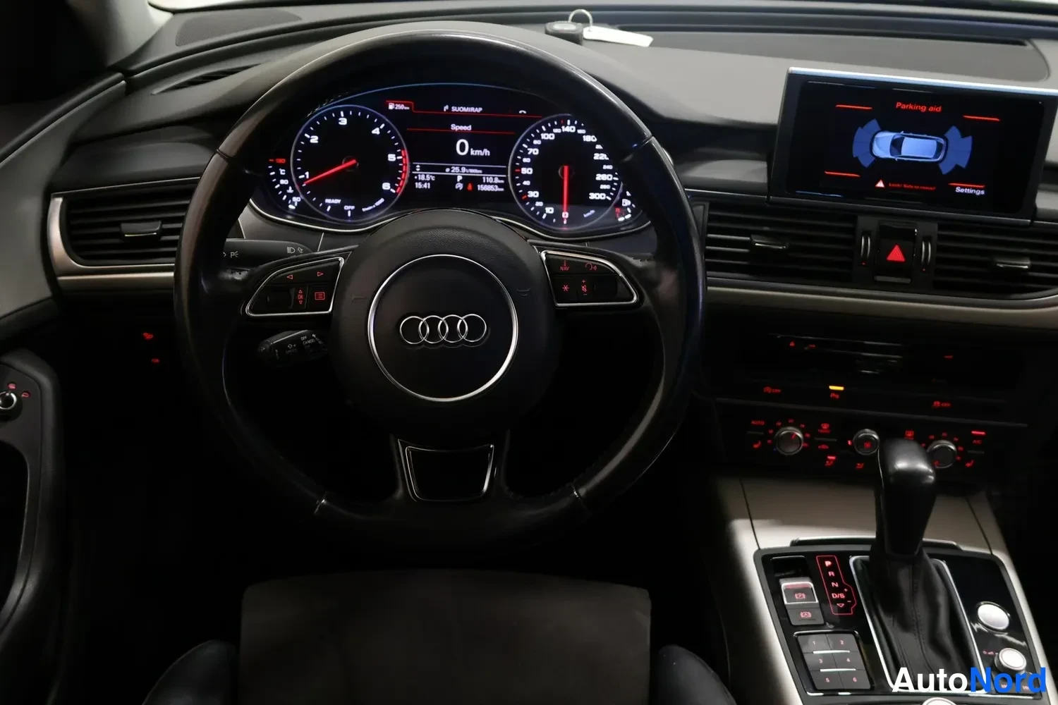 Yksityiskohta: Audi-ohjauspyörä, instrumenttikytkennät näkyvissä ja infotainment-näyttö, jonka teksti lukee Parking aid.