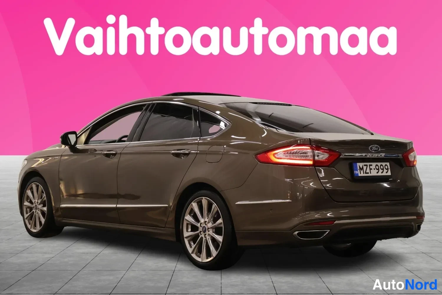 Takaviisto: Ruskean Ford Mondeo -sedanin takakulmanuvaus vasemmalta; rekisteritunnus, lasikatto ja halkeamattomat tai vagaliovarustettu. Takavalo sytytettynä.