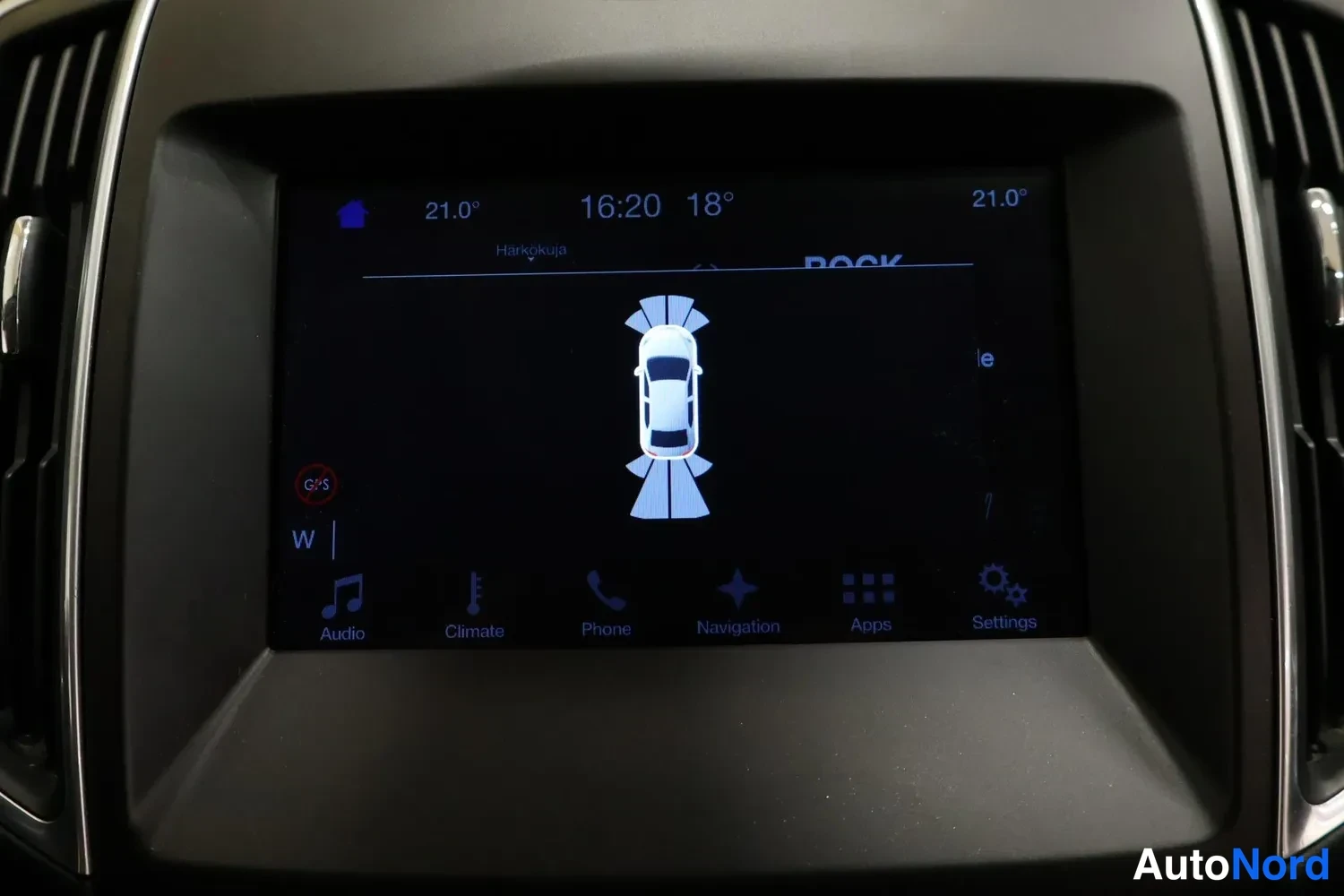 Yksityiskohta: Kojelaudan näyttö parkkitutkan kuvalla autosta ja tutkikaavioista; alavalikossa Audio, Climate, Phone, Navigation, Apps ja Settings.