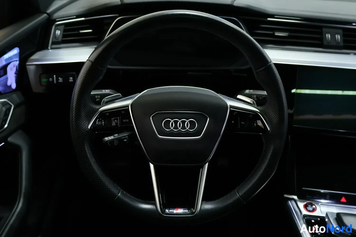Muu: Ohjaamossa Audi-merkkinen ohjauspyörä, kojelaudan ilmastointiaukot ja keskikonsolan näyttö osin näkyvissä.