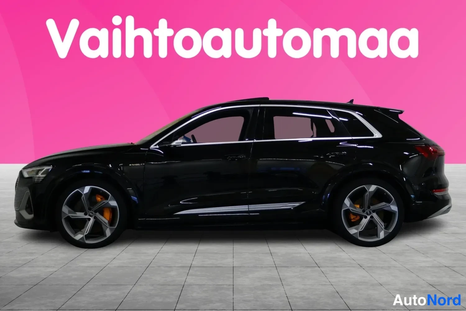 Etuviisto, nokka vasemmalle: Musta Audi e-tron S -maasturi sivusta etukulmasta, keula vasemmalla, suuret kevytmetallivanteet ja oranssit jarrusatulat näkyvissä.