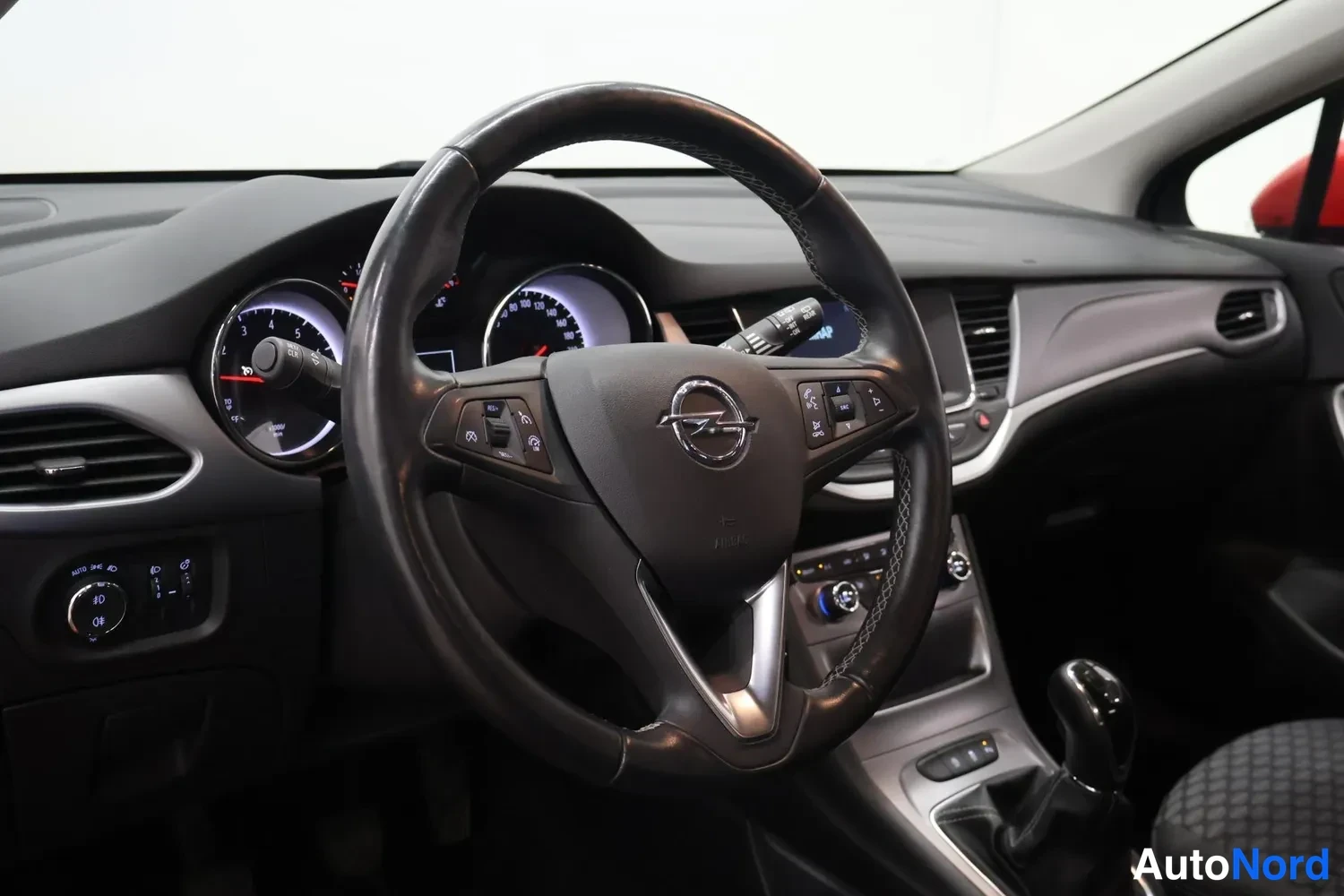 Muu: Kuljettajan puolen näkymä: Opel-ohjauspyörä, mittaristo ja keskikonsoli; vaihtokeksiä ja manuaalivaihteiston vaihtajan näkyy keskikonsolissa.