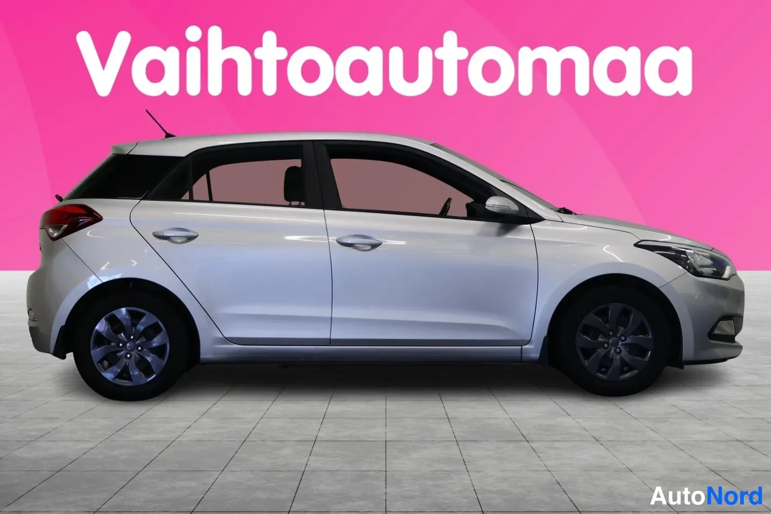 Sivulta: Hopeanharmaa 5-ovinen hatchback sivulta kuvattuna; tummat kevytmetallivanteet, peilit ja ovikkahvat nakyvat, rosa tausta.