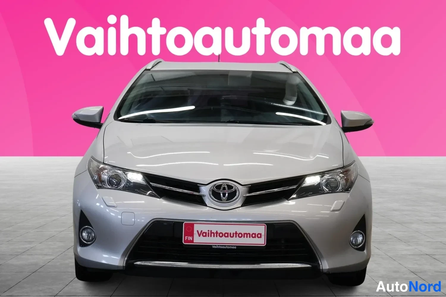 Edestä: Hopeanvärinen farmariauto suoraan edestä kuvattuna; etusäleikkö,Toyota-merkki, ajovalot ja etupuskuri näkyvissä.