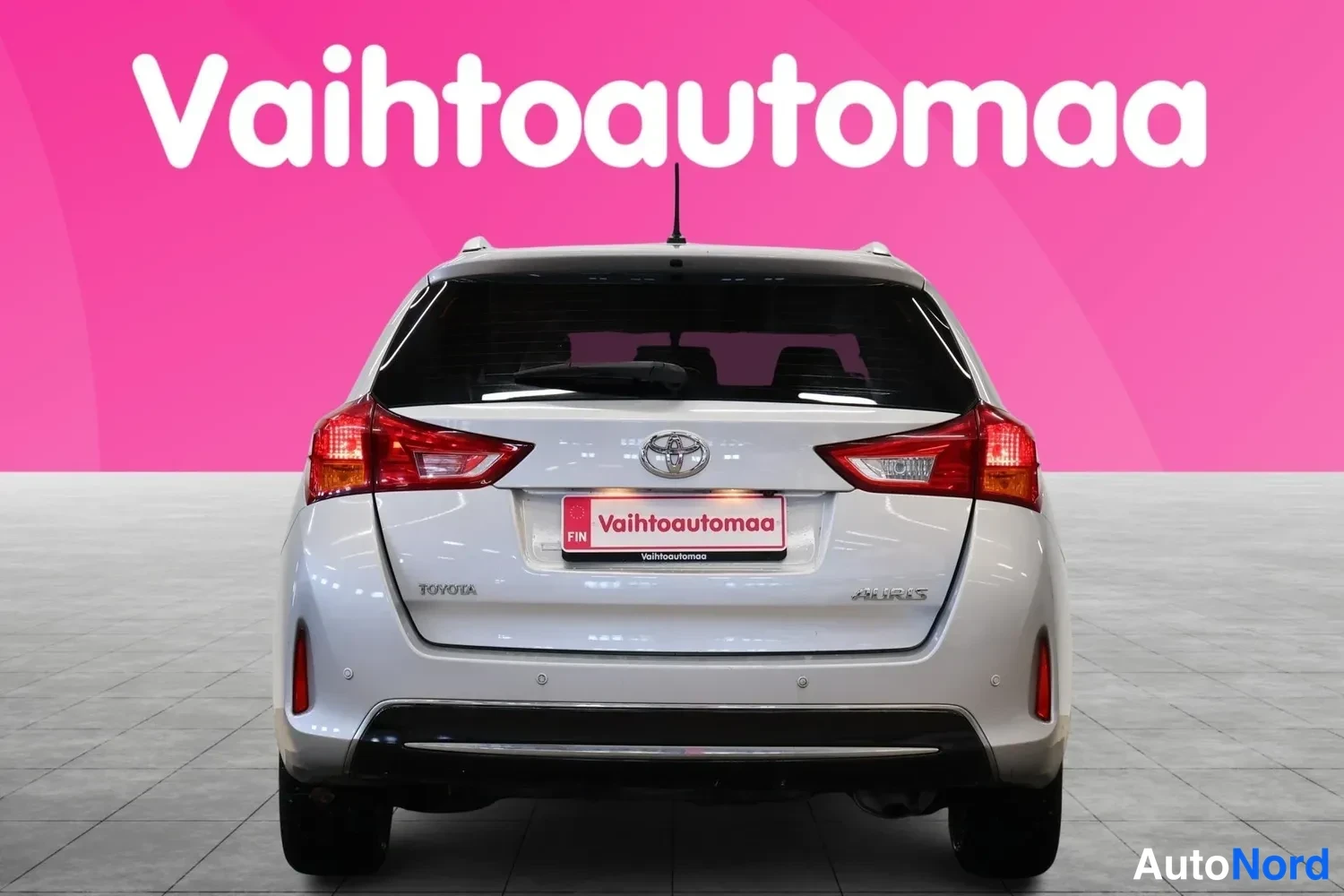 Takaa: Hopeanharmaan Toyota Auris -farmarin takaosa suoraan takaa, punaiset takavalot ja Vahtoautomaa-tunnus takaluukussa.