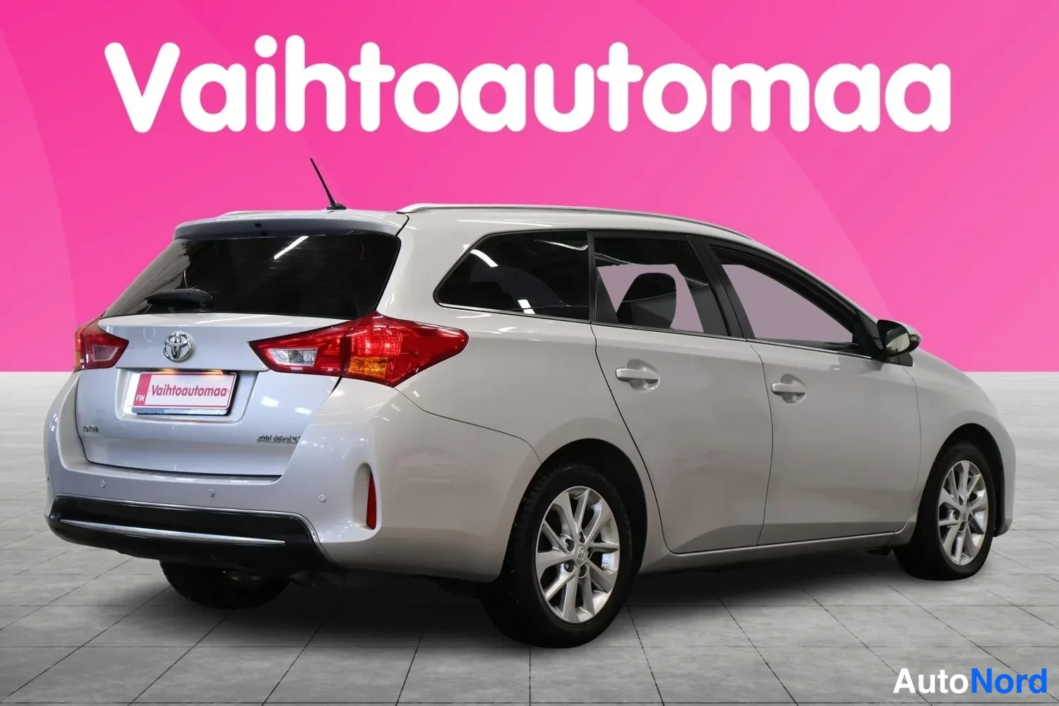 Takaviisto: Hopeanharmaan Toyota Auris -farmarin takaosa ja vasen kylki takaviistosta, takavalot kuvan vasemmassa reunassa.