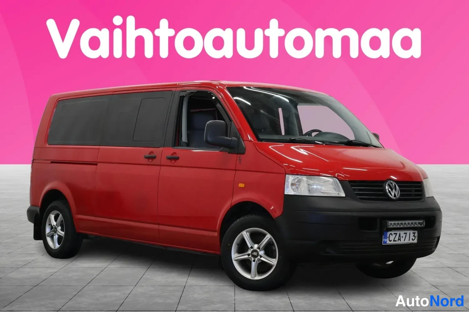 Etuviisto, nokka oikealle: Punainen Volkswagen Transporter -pakettiauto kolmesta neljäsosasta, keula oikealla.