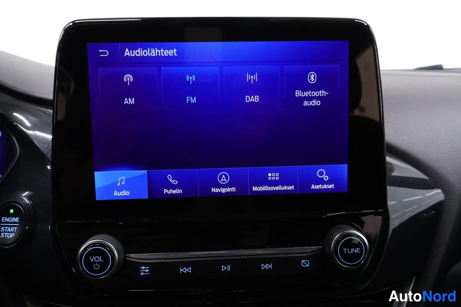Yksityiskohta: Audion lähdemenu ruudulla: AM, FM, DAB ja Bluetooth-audio, alla valikkorivi ja VOL- ja TUNE-säätimet.