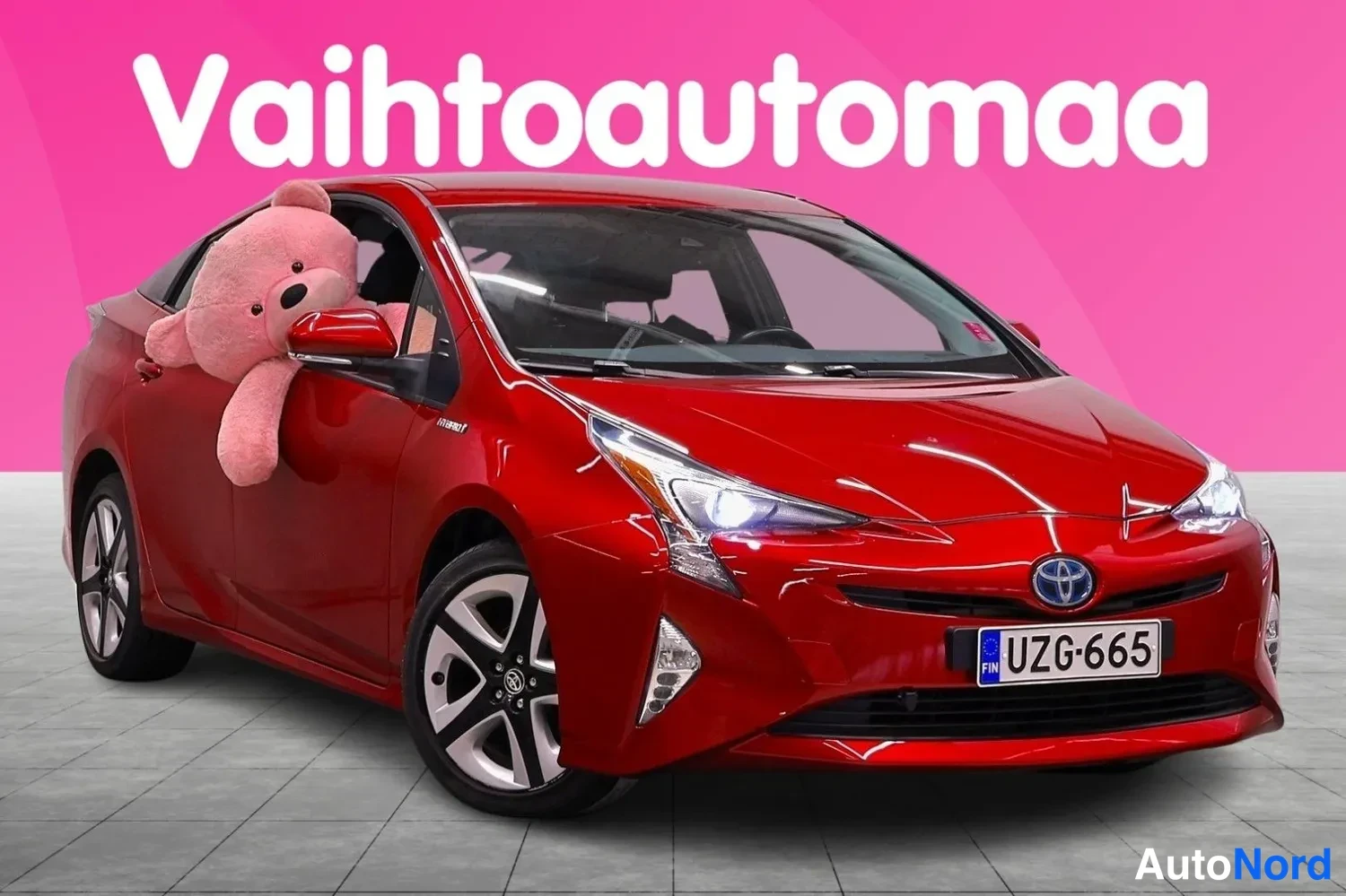 Etuviisto, nokka oikealle: Punainen Toyota Prius edestä oikealta kuvattuna, rekisteritunnus, vaaleassa studiossa vaaleanpunainen tausta ja teksti Vaihtoautomaa.