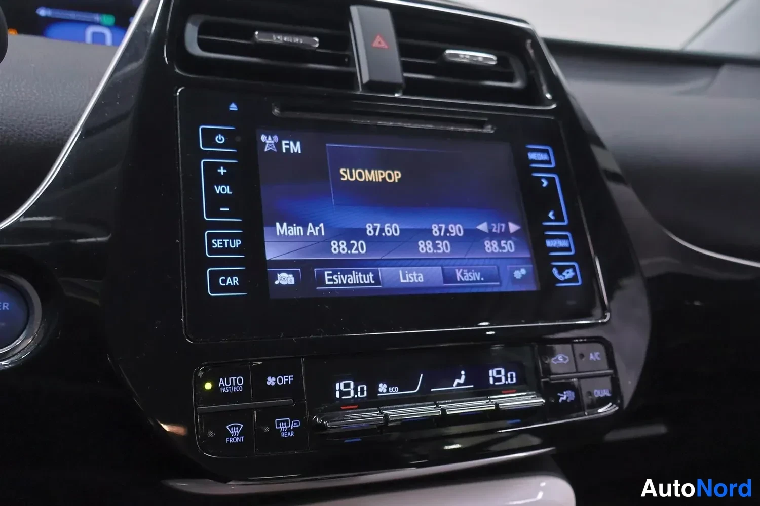 Muu: Kojelaudan keskusnäyttö näyttää FM-radiota (SUOMIPOP) taajuusluettelolla, alla ilmastointipaneeli DUAL- ja A/C-painikkeilla sekä molemmin puolin 19,0 asteen ase