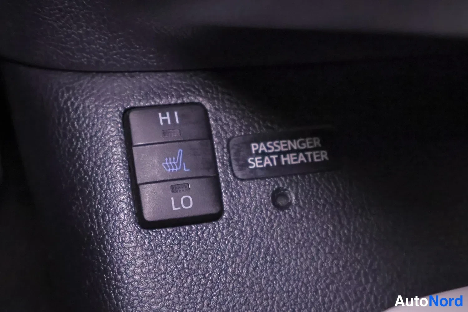 Muu: Tummasta muovipaneelista lähikuva istuimenlämmittimen kytkimestä HI/LO-asemilla ja kyltillä 'PASSENGER SEAT HEATER'.