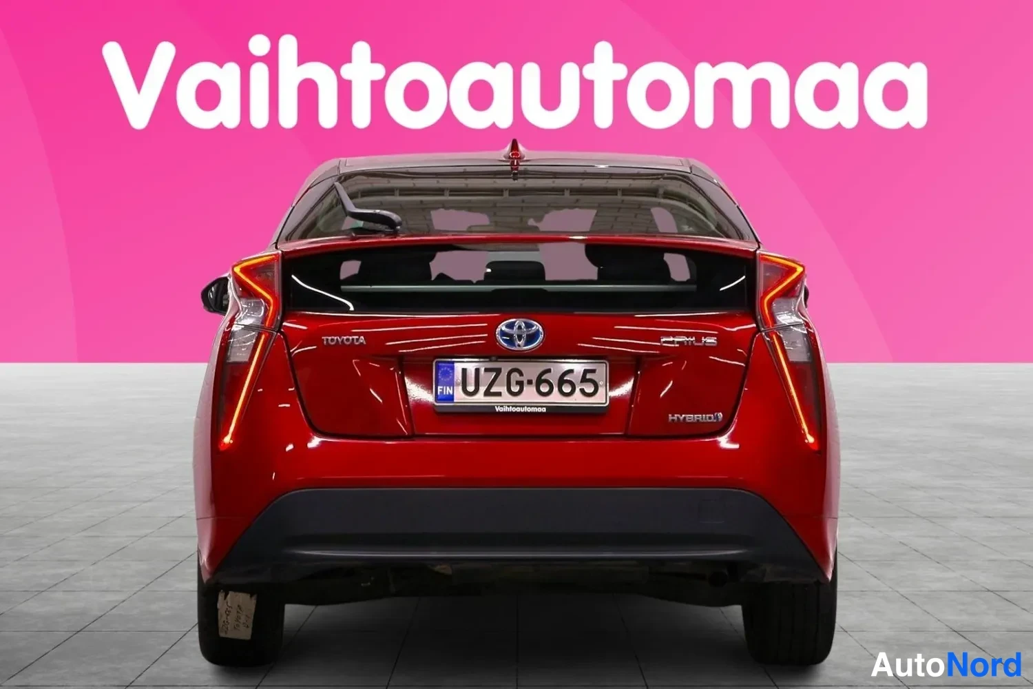 Takaa: Punainen Toyota Prius suoraan takaa, rekisteritunnus, takakonepellissä Toyota-, Prius- ja Hybrid-merkinnät.