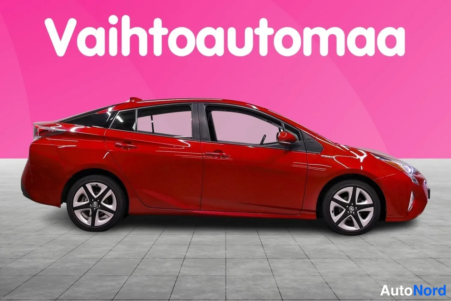 Sivulta: Punaisen Toyota Priuksen sivuprofiili molemmat kyljet näkyvät studiossinisellä taustalla.