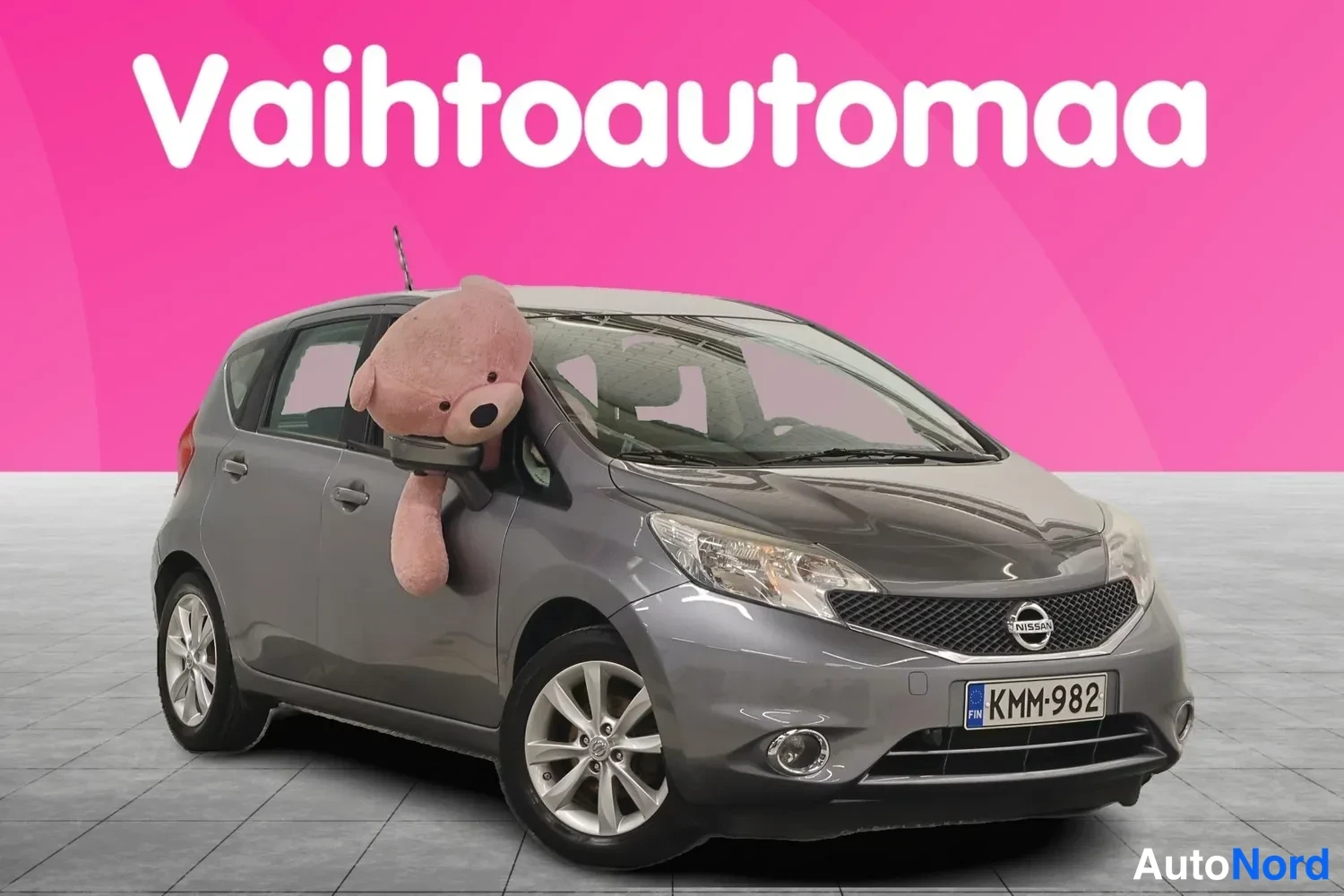 Etuviisto, nokka oikealle: Nissan Note -henkilöauto harmaana etukulmasta oikealta, rekisterikilpi, studiossa vaaleanpintaisella lattialla.