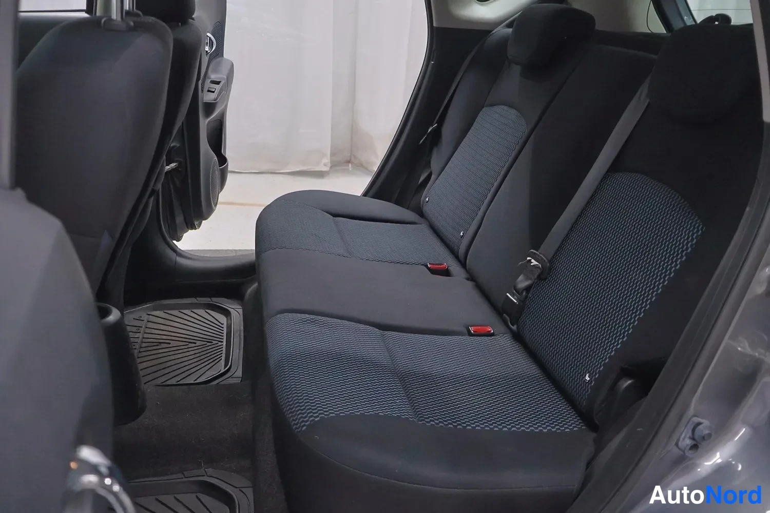 Muu: Nissan Note 2014: takapenkkien tummat kangasistuimet takaa päin avatusta takaluukasta, mustat kumimatot lattialla.