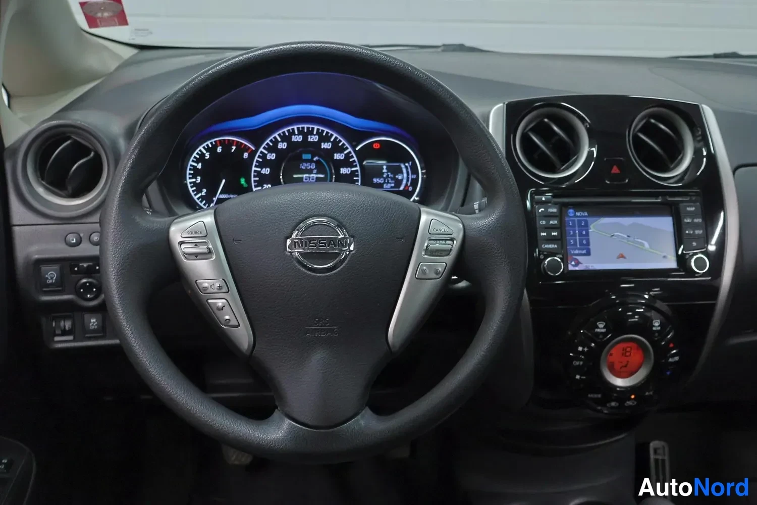 Yksityiskohta: Ohjauspyörä ja mittaristo lähikuvassa, Nissan-merkki ohjauspyörässä ja radio-näyttö keskikonsolissa.