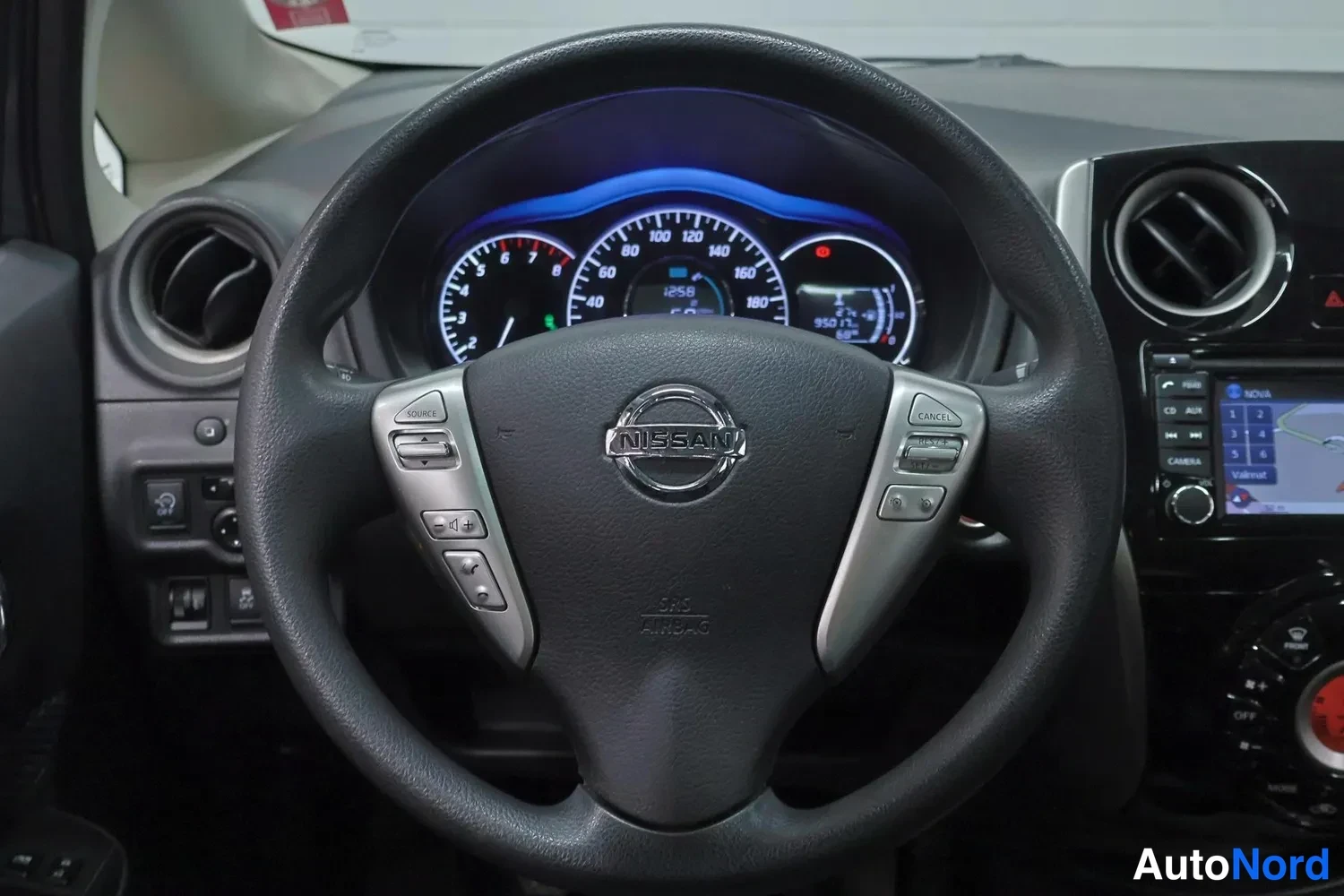 Yksityiskohta: Nissan-ohjauspyörä ja mittaristo etualalla, taustalla kosketusnäytöllinen radio / navigaatio ja ilmastointiautomaatin A/C-ohjain.