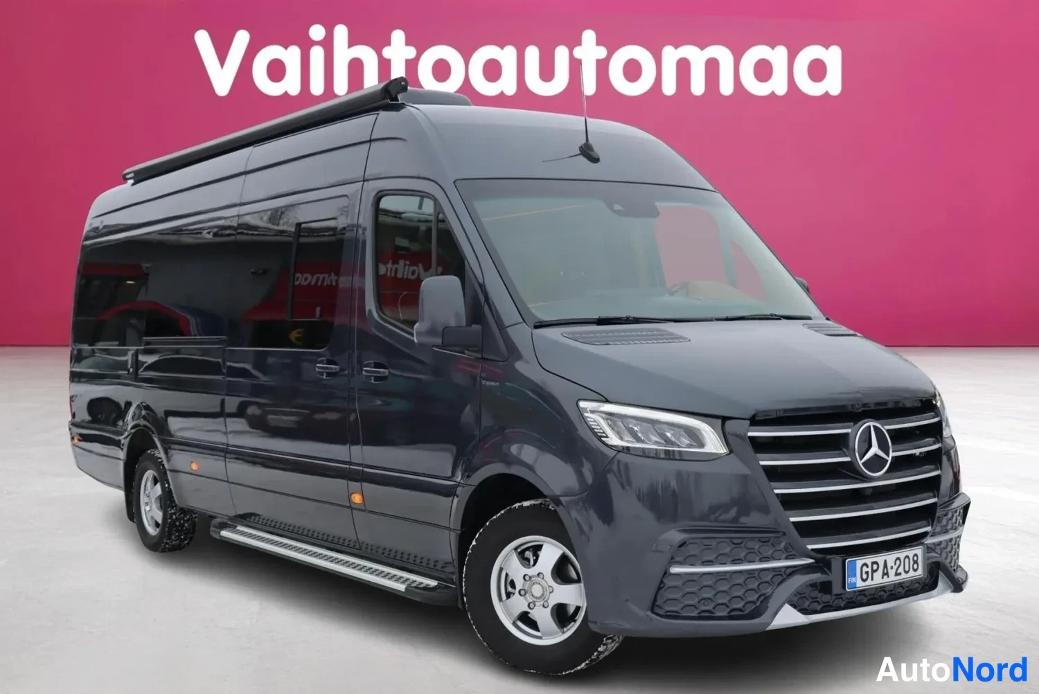 Etuviisto, nokka oikealle: Mercedes-Benz Sprinter -pakettiauto etuviistosta, keulan osoittaessa oikealle, tummanharmaa koripinta ja kattoon asennettu kaiutin.