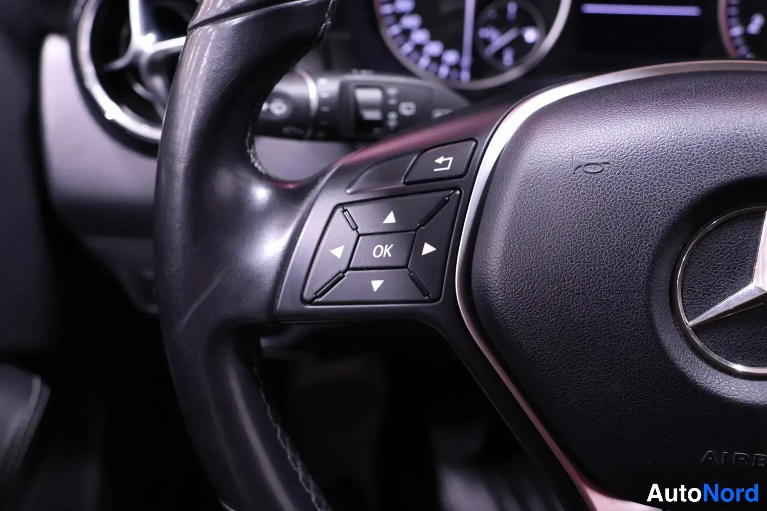 Muu: Ohjauspyörän vasen puhallus ja nappiryhmä, jossa OK-painike ja nuolinäppäimet, Mercedes-tähti keskellä ja AIRBAG-teksti.
