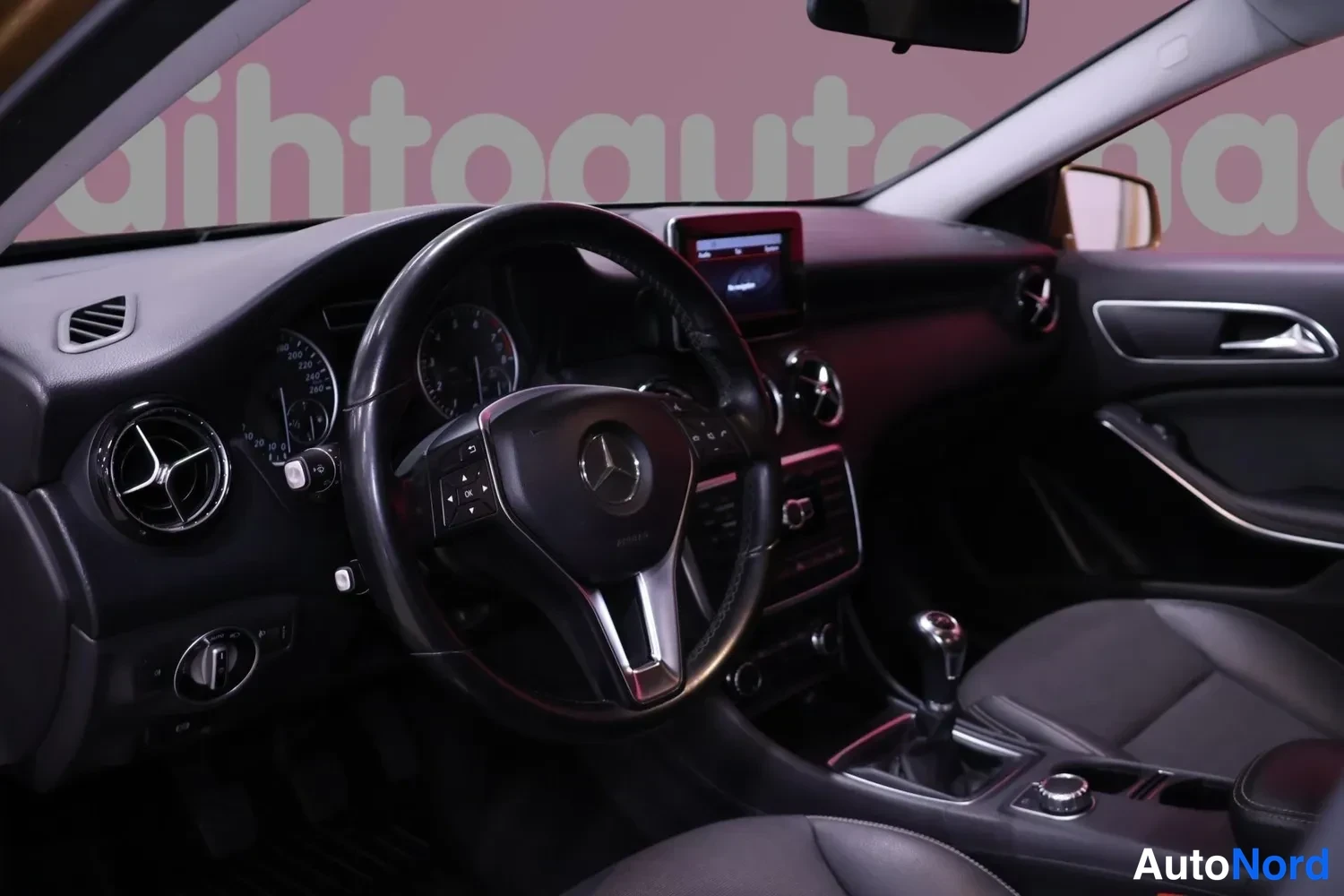 Muu: Mercedes-Benzin ohjaamo: ohjauspyörä, mittaristo, kojelauta ja vaihtaja näkyvät tummassa sisätilassa.