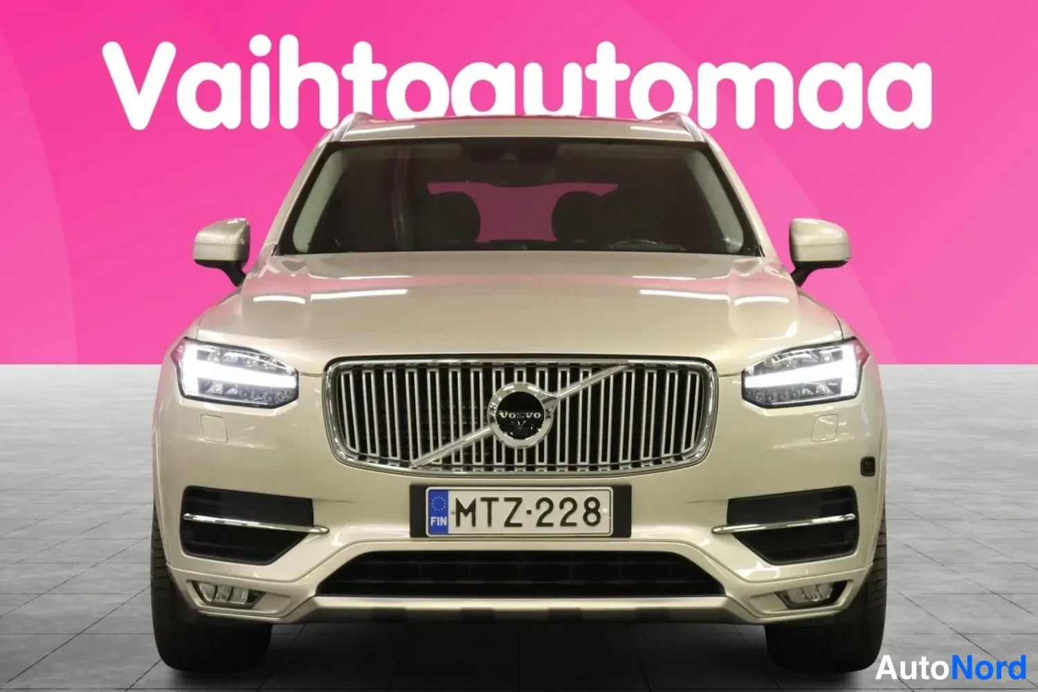 Edestä: Beige Volvo XC90 suoraan edestä, etusäleikkö ja Volvo-merkki näkyvissä, rekisteritunnus.