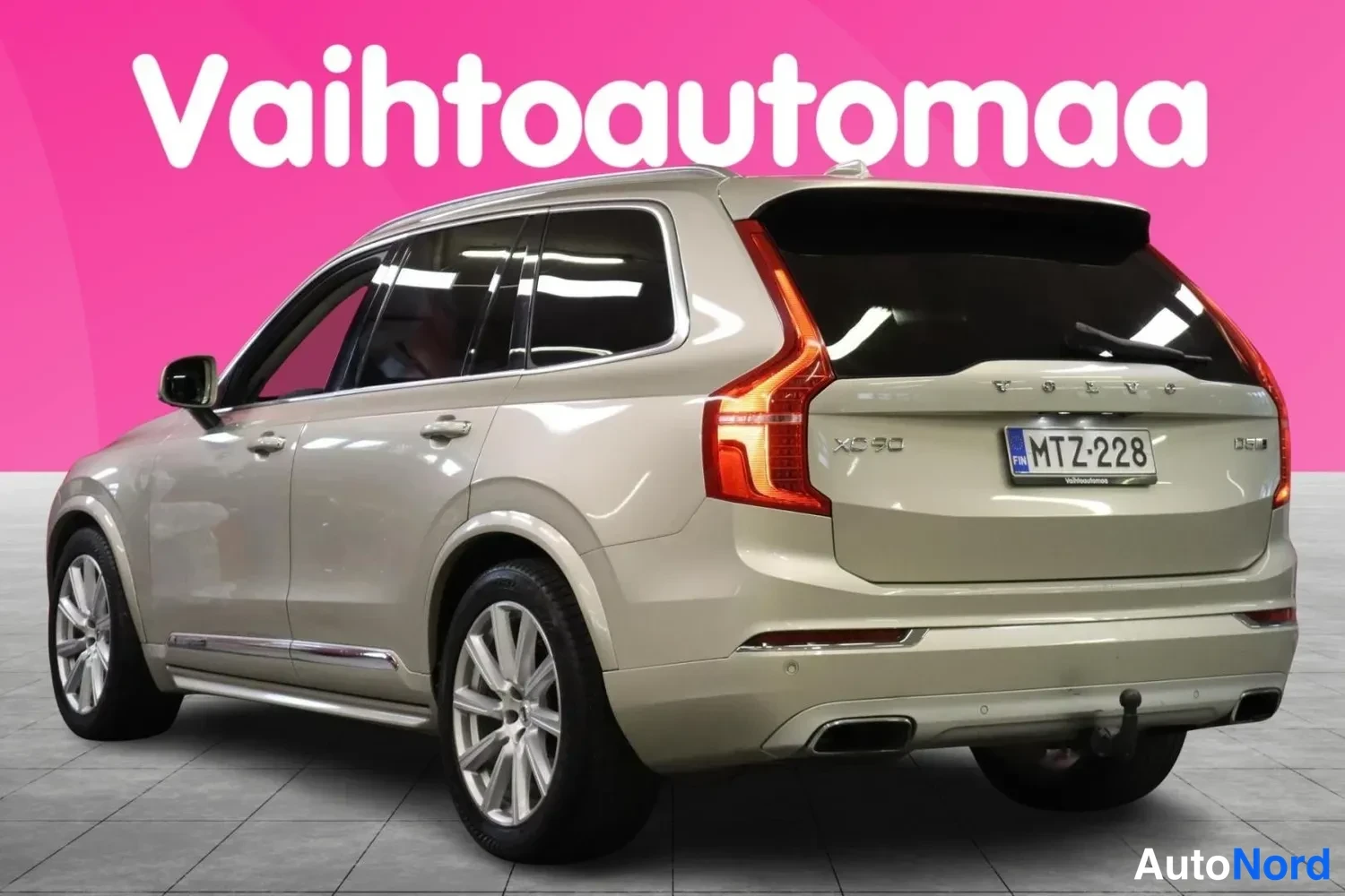 Takaviisto: Beigeaiheisen farmarimallisen automobiilin takaosasta vasemmalta kuvattu kolmen neljäsosan näkymä; XC90-merkintä, -rekisterikilpi ja vetokoukku näkyvät.