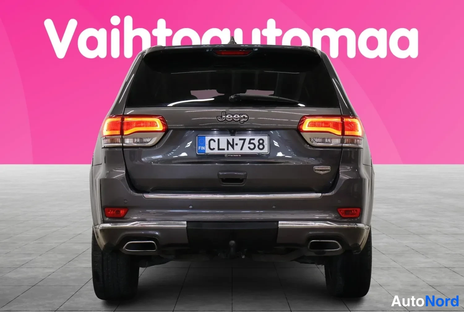 Takaa: Auton takaosa suoraan takaa: Jeep-merkki, rekisterikilpi, kaksoispakoputket ja perävaunukoukun kiinnitys näkyvät.
