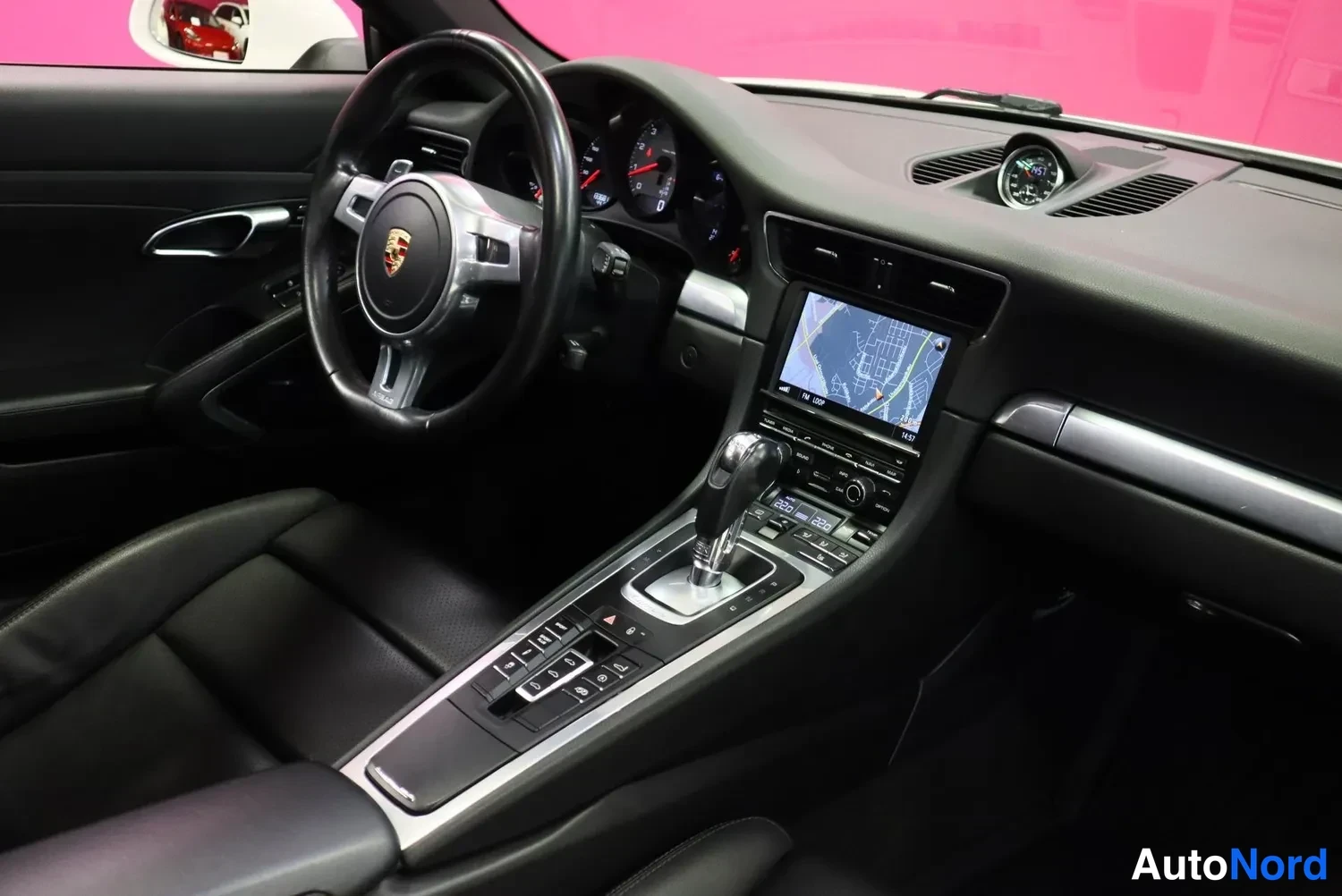 Edestä: Auton sisätilat: Porsche-ohjauspyörä, mittaristo, navigointinäyttö ja automaattivaihteen valitsin keskikonsolissa.