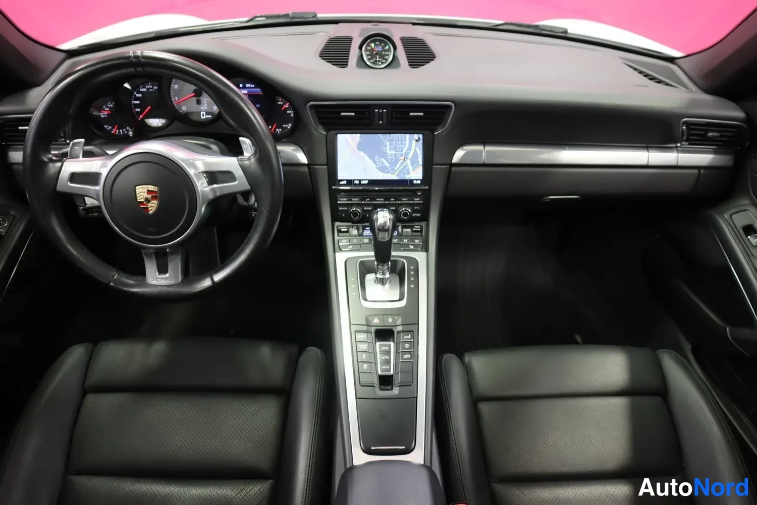 Edestä: Kojetaulu ja etuistuimet ylhäältä: Porsche-ohjauspyörä, karttanyttö, automaattivaihteen valitsin ja kaksi mustaa istuinta.