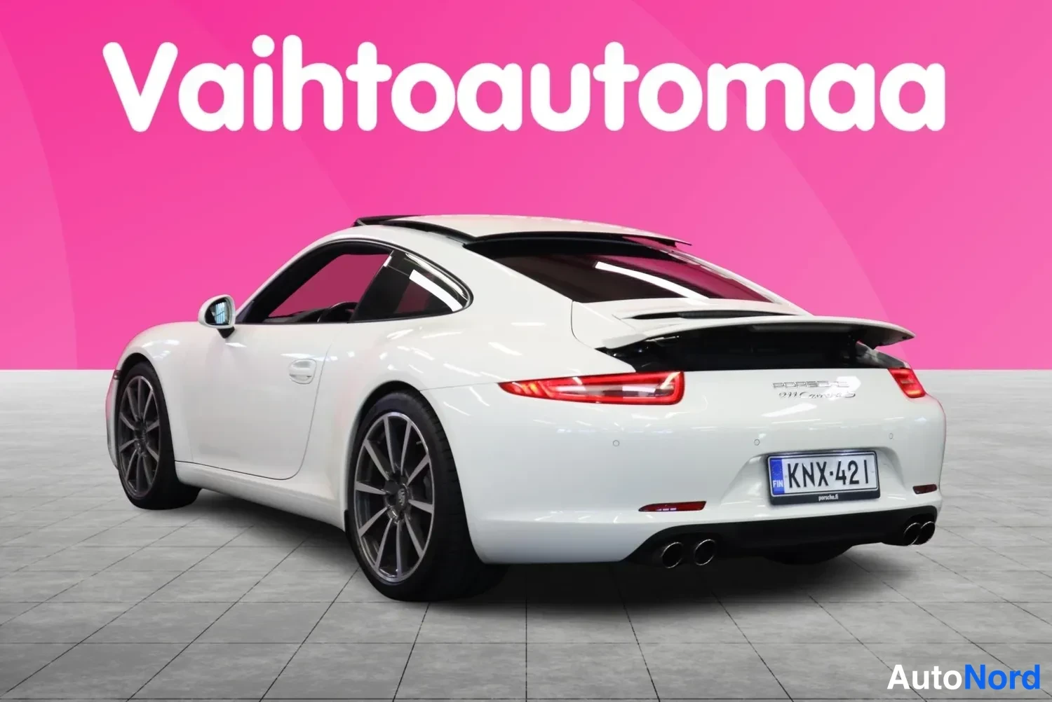 Takaviisto: Porsche 911:n takaviistokuva vasemmalta: valkoinen coupe, nouseva takasiipi, neljä pakoputkea, rekisterikilpi, pinkki tausta.