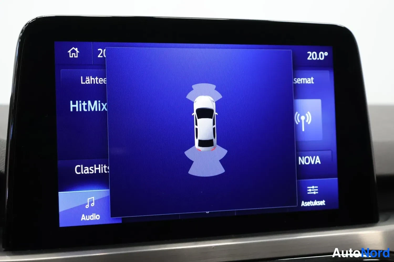 Muu: auton kojelaudan infotainment-näyttö, jossa näkyy pysäköintianturien kuvake ja radiovalikko.